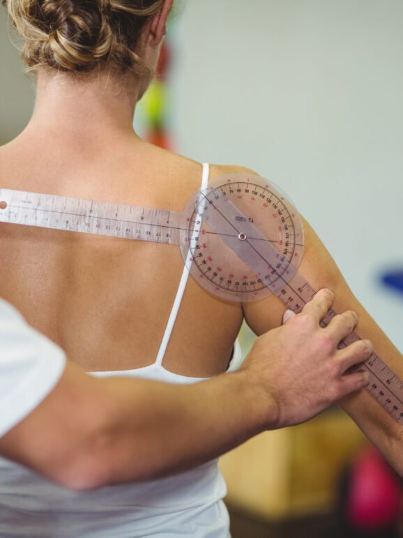 Male therapist measuring female patient back with goniometer in clinic
