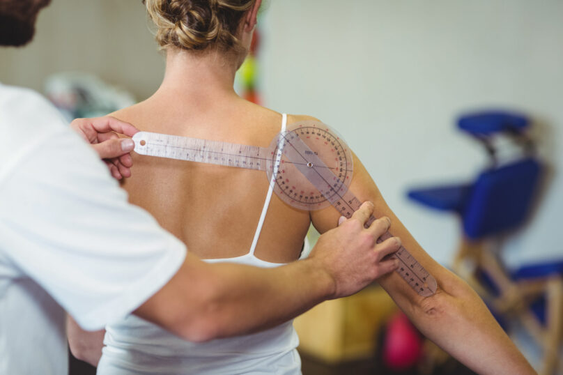 Male therapist measuring female patient back with goniometer in clinic