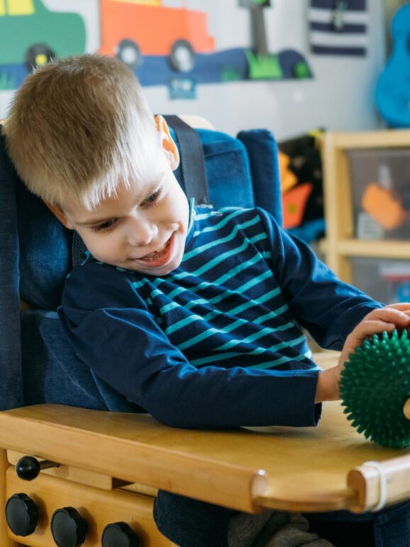 Sensory Activities for kids with disabilities. Preschool Activities for Children with Special Needs. Boy with with Cerebral Palsy in special chair play with mom at home
