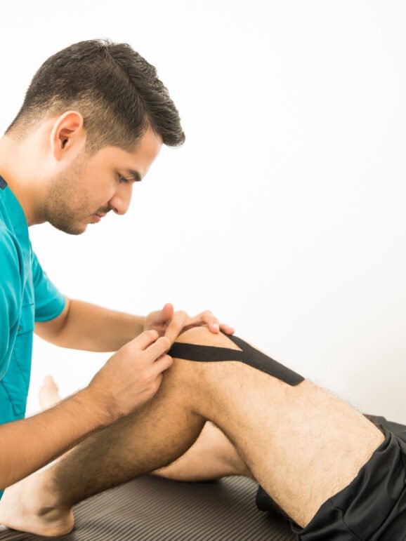 Young physiotherapy professional applying KT Tape on athlete's knee in hospital